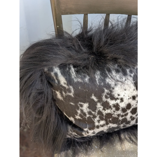 A plush black icelandic sheepskin throw with long wool draped over a cowhide pillow with white and dark brown spots