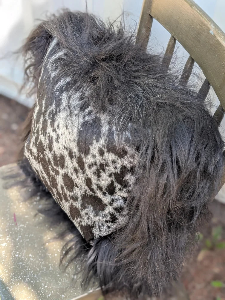 A plush spotted cowhide pillow with black and white icelandic sheepskin and long wool shaggy trim