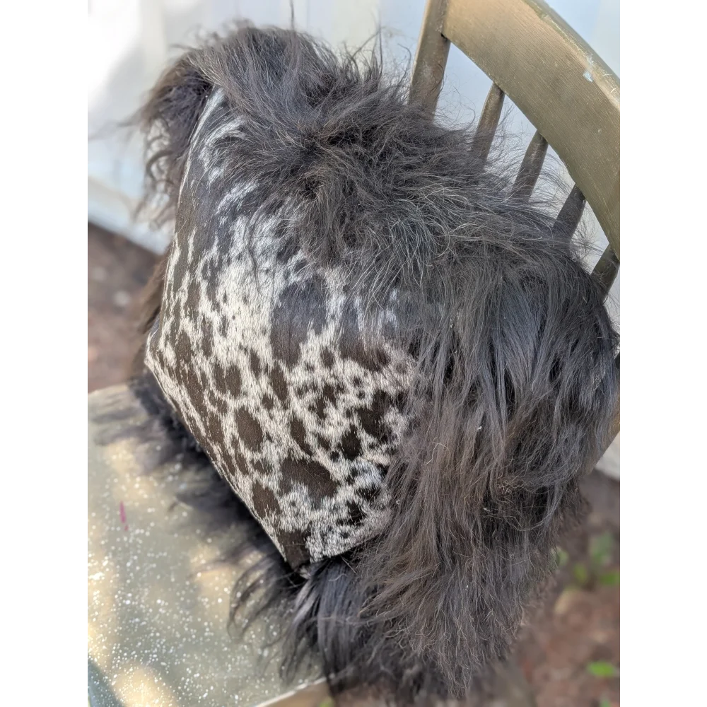 A plush spotted cowhide pillow with black and white icelandic sheepskin and long wool shaggy trim