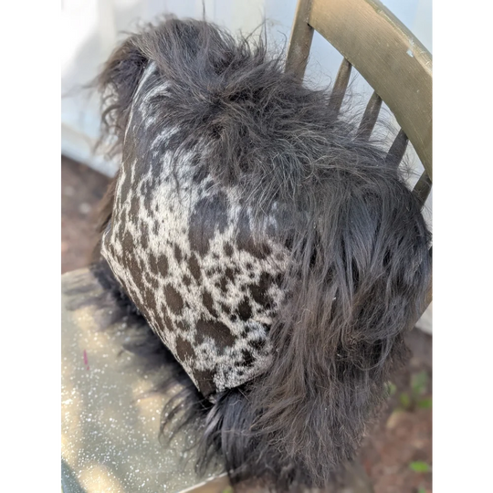 A plush spotted cowhide pillow with black and white icelandic sheepskin and long wool shaggy trim