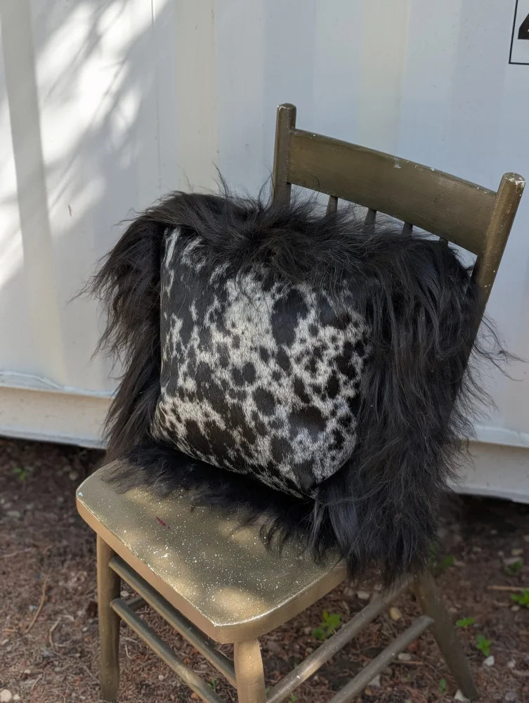 Spotted cowhide pillow with black and white spots and long black icelandic sheepskin wool trim perfect for cozy decor