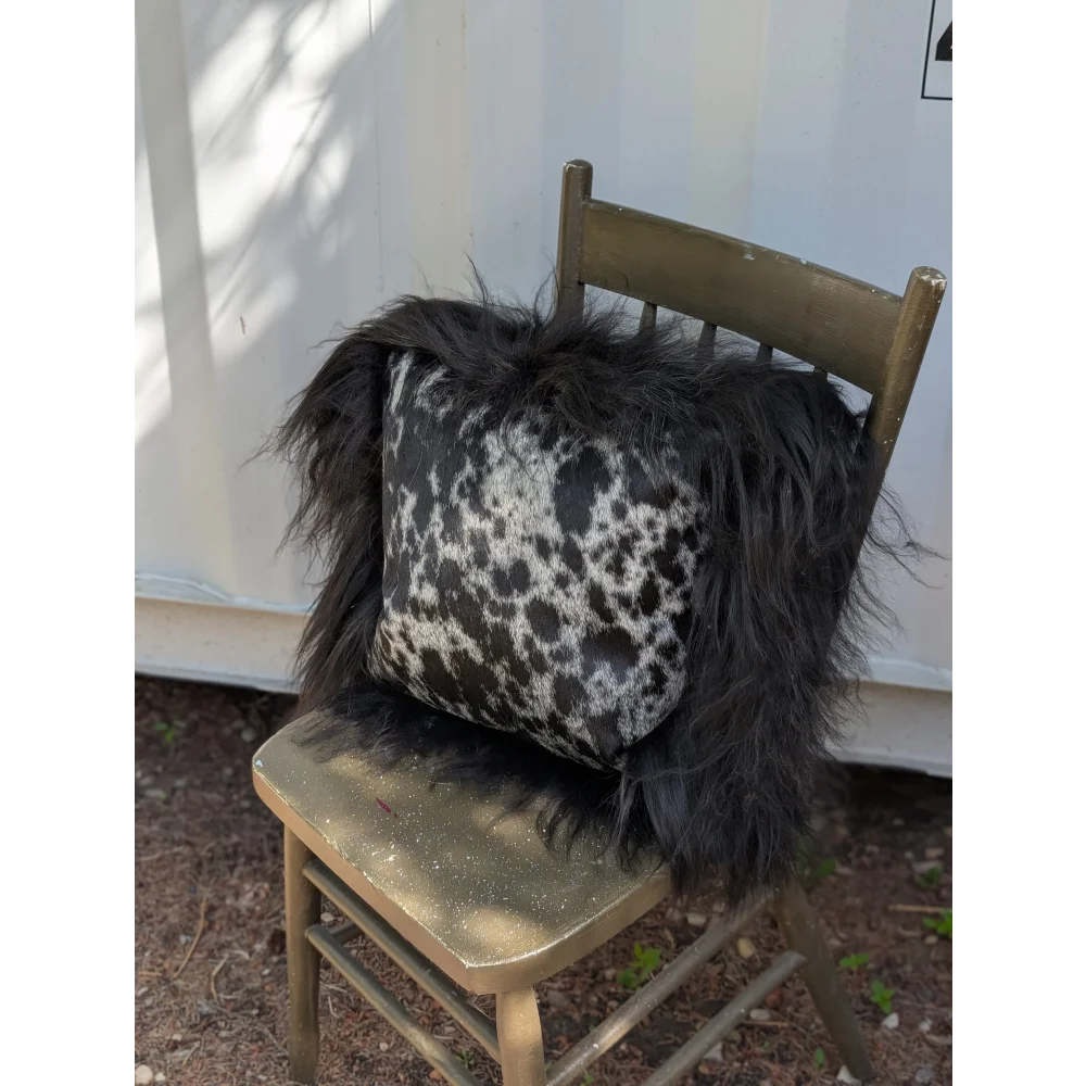 Spotted cowhide pillow with black and white spots and long black icelandic sheepskin wool trim perfect for cozy decor