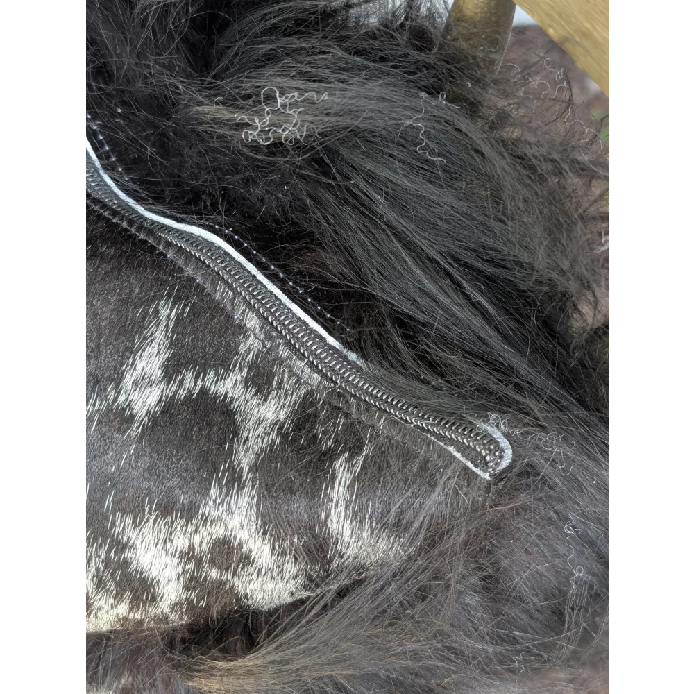 A silver-toned zipper runs along the edge of dark spotted cowhide with natural black icelandic sheepskin markings