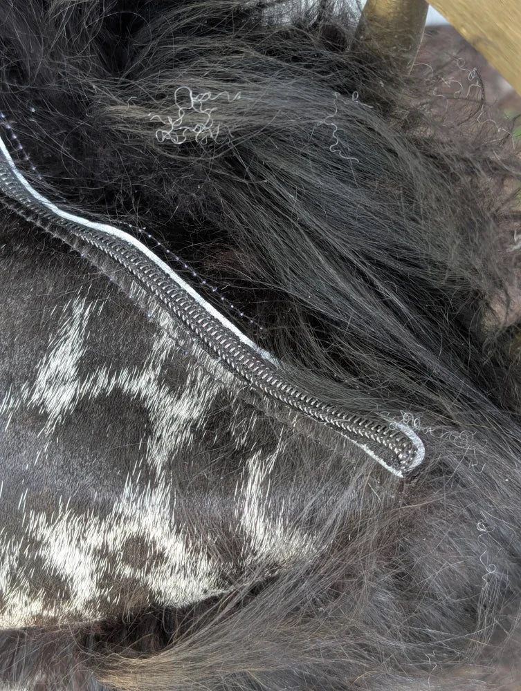 A silver-toned zipper runs along the edge of dark spotted cowhide with natural black icelandic sheepskin markings