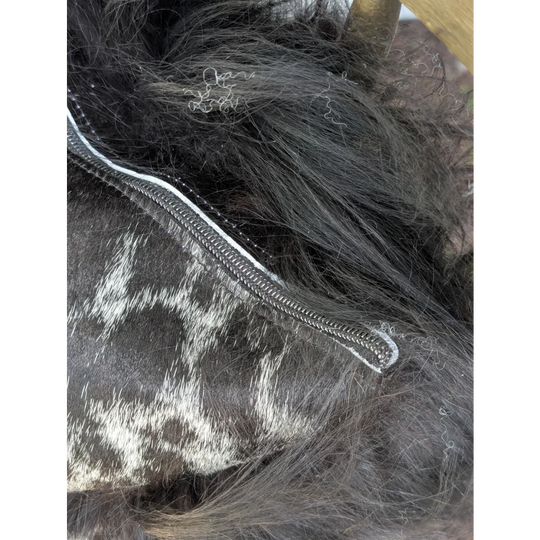 A silver-toned zipper runs along the edge of dark spotted cowhide with natural black icelandic sheepskin markings