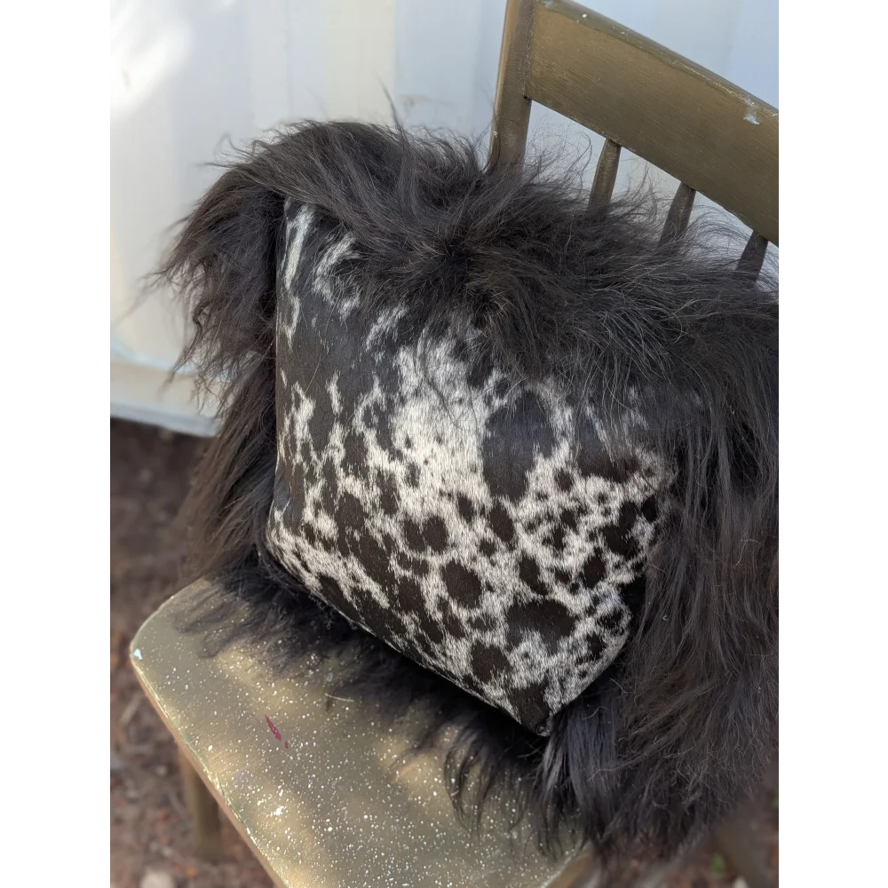 A plush spotted cowhide pillow with natural black icelandic sheepskin long wool trim for cozy decor