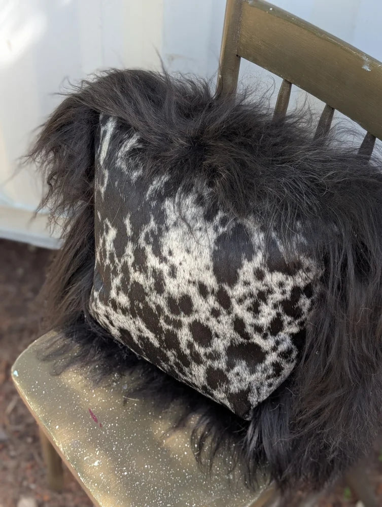 A plush spotted cowhide pillow with natural black icelandic sheepskin long wool trim for cozy decor