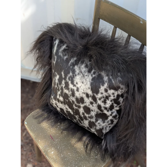 A plush spotted cowhide pillow with natural black icelandic sheepskin long wool trim for cozy decor