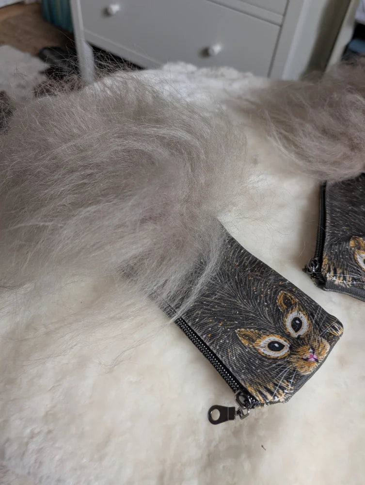 A gray fluffy sheepskin tail rests on a black cotton canvas squirrel coin purse with a cat face illustration