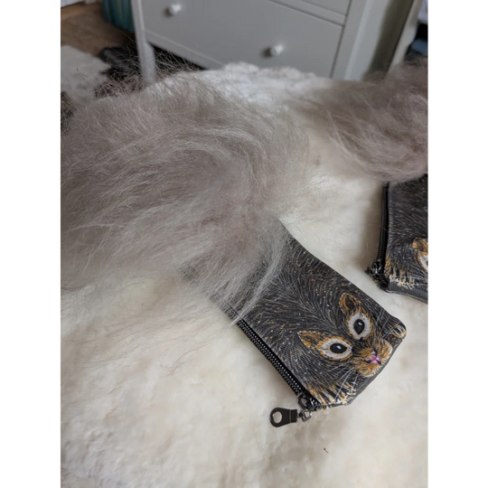 A gray fluffy sheepskin tail rests on a black cotton canvas squirrel coin purse with a cat face illustration