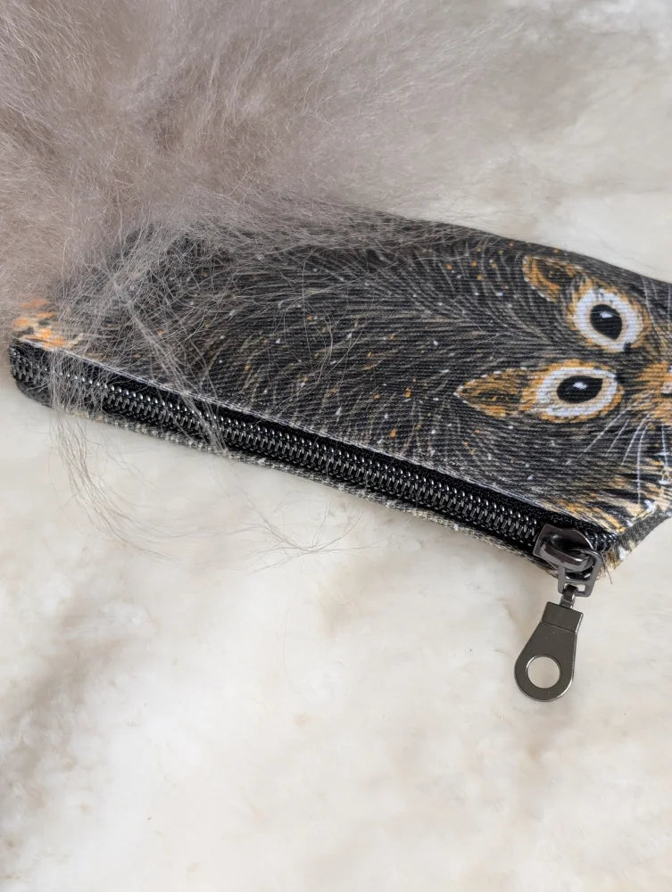 Black cotton canvas coin purse with embroidered squirrel face and sheepskin tail resting on soft gray fur
