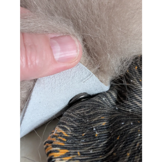 A light gray leather patch with black button on a cotton canvas squirrel coin purse with sheepskin tail fur