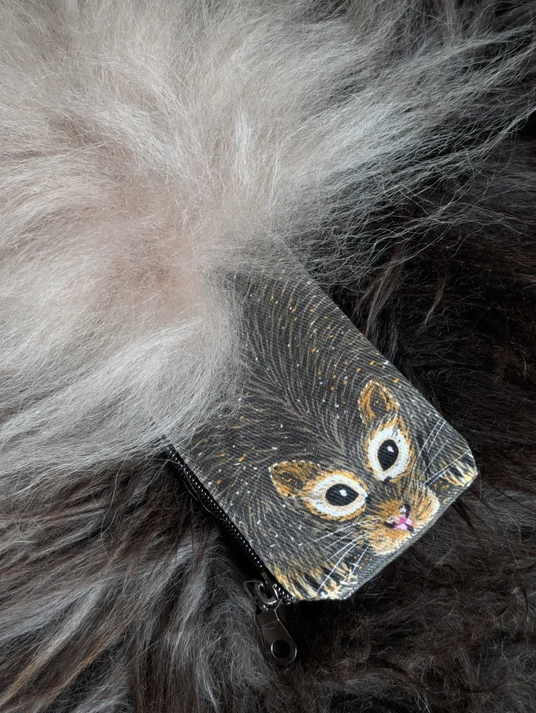 A small black cotton canvas coin purse with a cat face illustration and a fluffy sheepskin tail charm