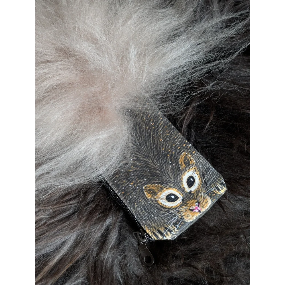 A small black cotton canvas coin purse with a cat face illustration and a fluffy sheepskin tail charm
