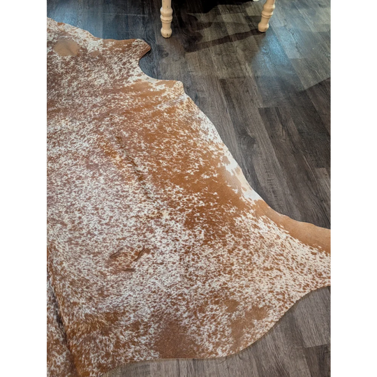 Large cowhide brown and white speckled rug with unique characteristics lying flat on dark wood floor beautiful rugs