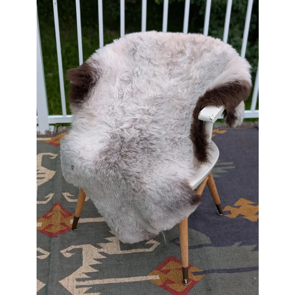A plush light gray and brown icelandic sheepskin rug with long wool draped over a white chair by angus oliver