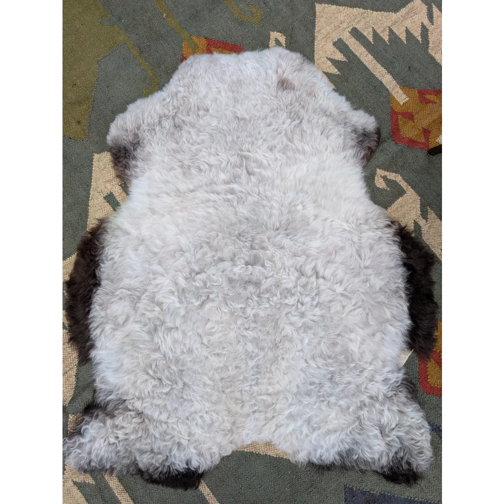 A plush curly white icelandic sheepskin rug with dark brown edges on a patterned carpet by angus oliver