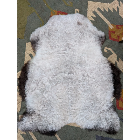 A plush curly white icelandic sheepskin rug with dark brown edges on a patterned carpet by angus oliver
