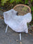 A cozy fluffy gray icelandic sheepskin rug draped over a wicker chair with white metal legs perfect for home decor