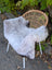 A soft gray wool icelandic sheepskin rug draped over a woven wicker chair with white metal legs