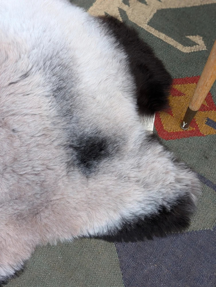 A plush white and black long wool icelandic sheepskin rug with natural texture by angus oliver measuring 43.5 by 33 inches