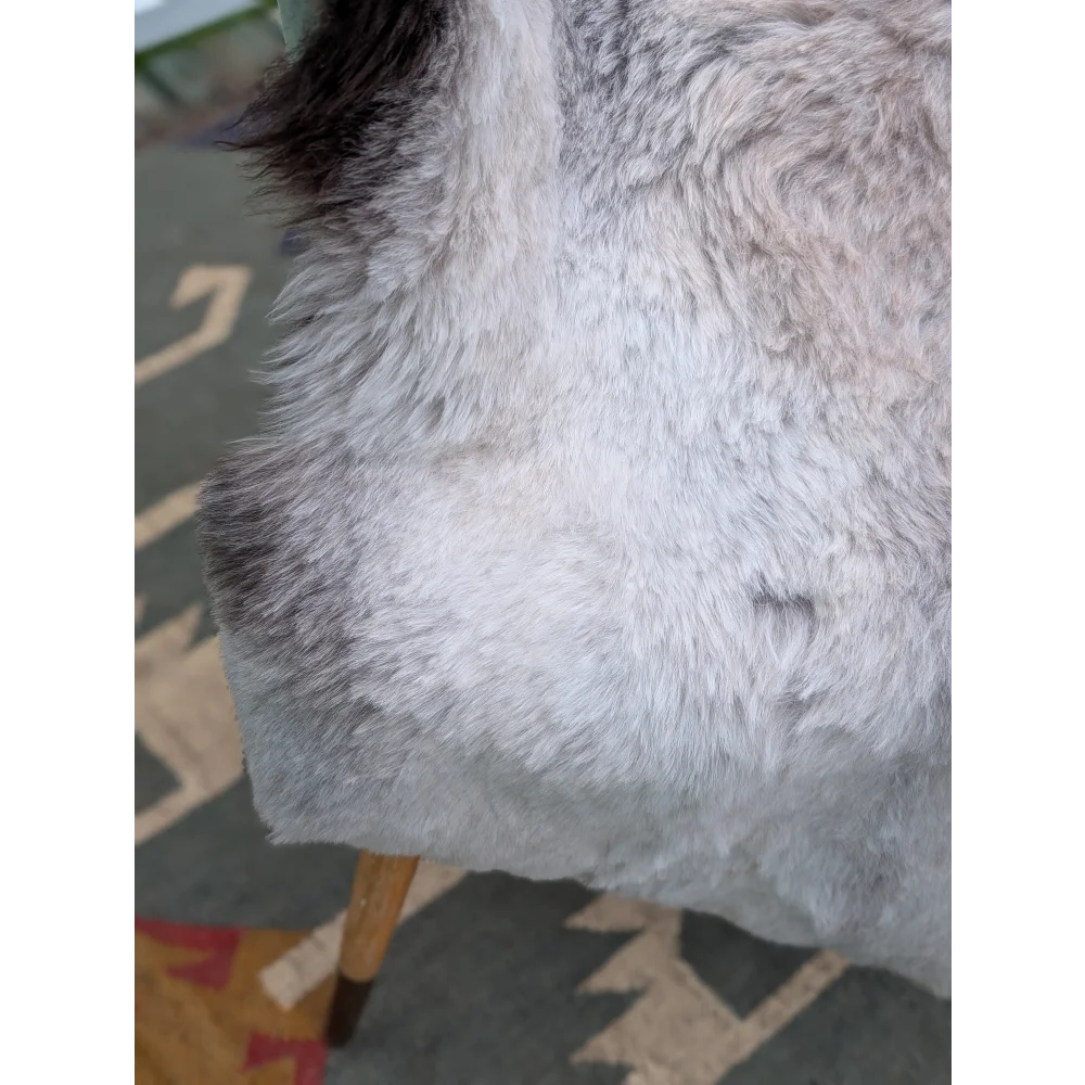 A plush gray faux fur chair with dark brown wooden legs featuring soft long wool icelandic sheepskin by angus oliver