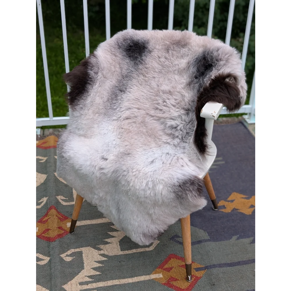 A plush gray and black long wool icelandic sheepskin rug draped over a white chair with wooden legs by angus oliver