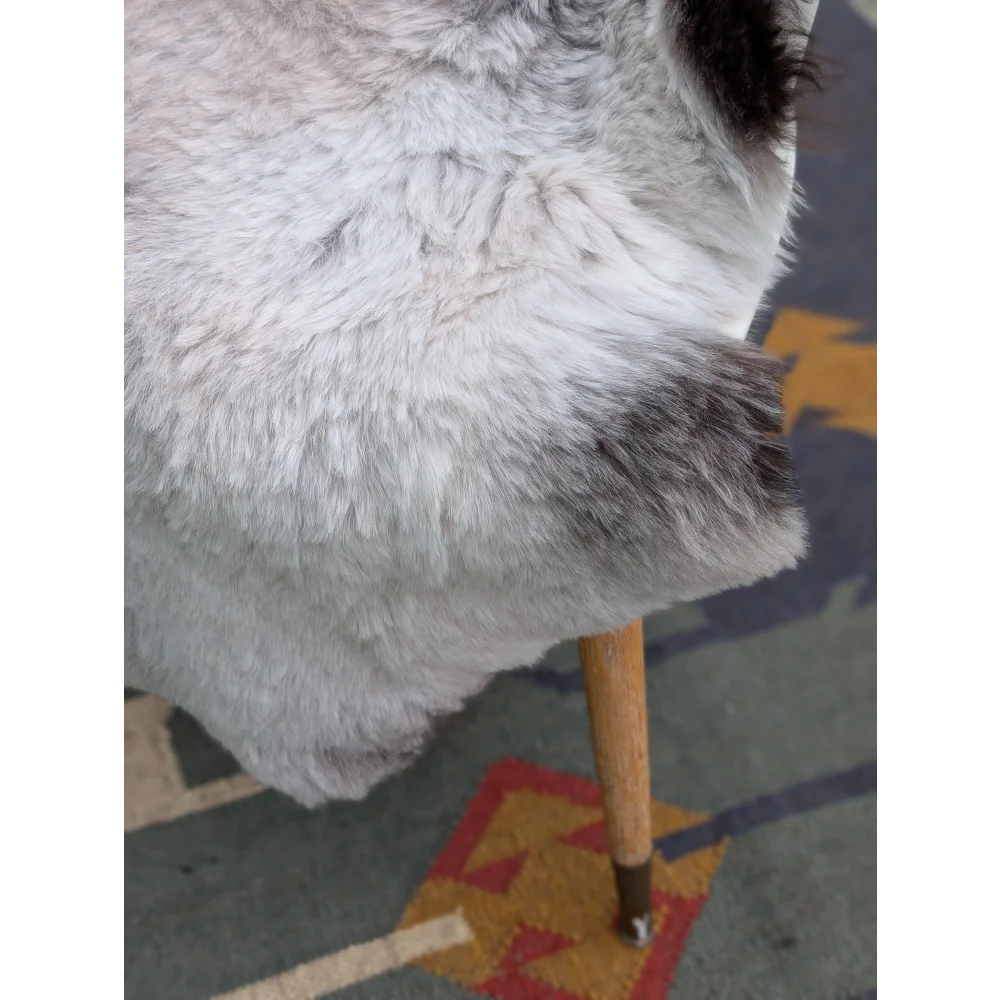 A plush gray and white icelandic sheepskin throw with long wool draped over a wooden chair leg by angus oliver
