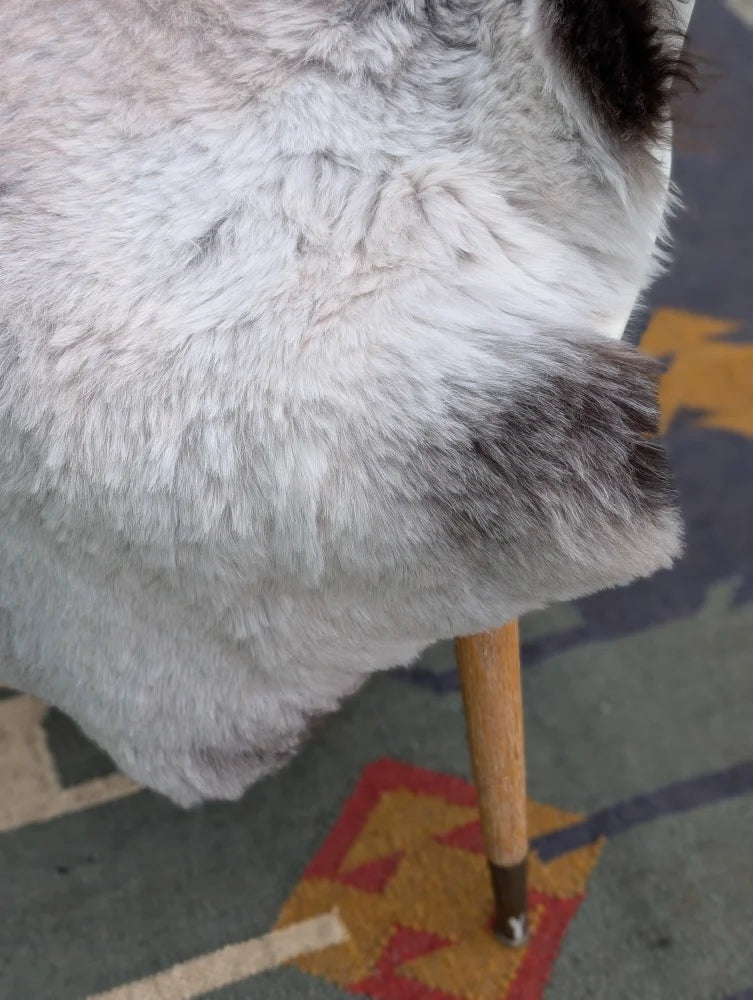 A plush gray and white icelandic sheepskin throw with long wool draped over a wooden chair leg by angus oliver