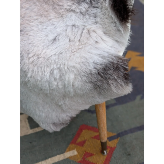 A plush gray and white icelandic sheepskin throw with long wool draped over a wooden chair leg by angus oliver