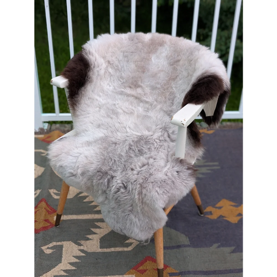 A large icelandic sheepskin rug in soft gray with dark brown patches draped over a white wooden chair by angus oliver