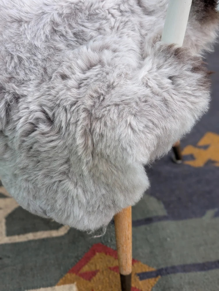 A plush light gray long wool icelandic sheepskin throw draped over a wooden chair leg by angus oliver