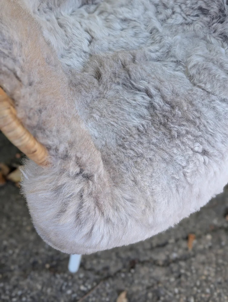 A plush light gray icelandic sheepskin cushion with soft long wool icelandic texture and natural dark edges