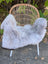 A soft light gray large icelandic sheepskin with long wool and dark edges draped over a wicker chair with white metal legs