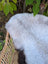 A large 44 x 27 white long wool icelandic sheepskin rug with dark edges rests in a woven wicker basket