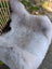 A soft gray icelandic sheepskin rug with long wool and dark edges draped over a wicker chair for cozy style