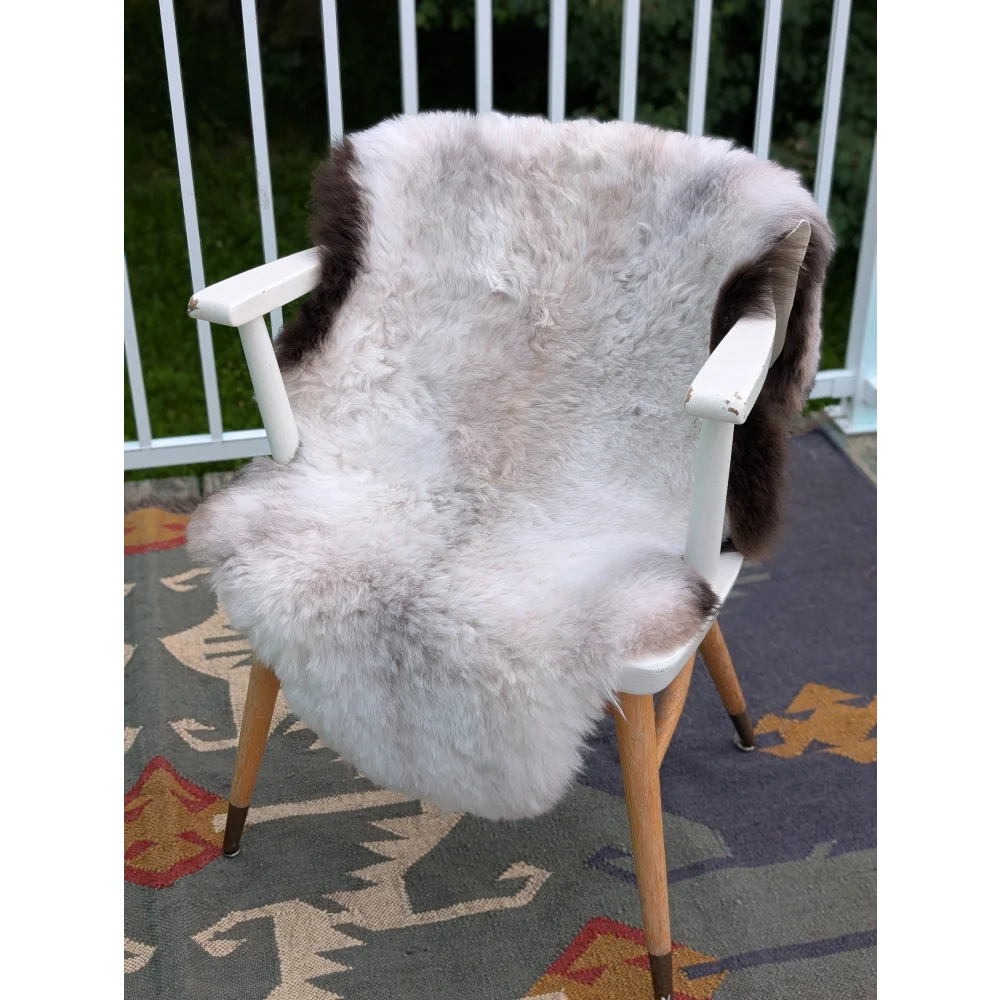 A plush large icelandic sheepskin throw with long wool grayish-brown patches draped on a minimalist chair back by angus oliver