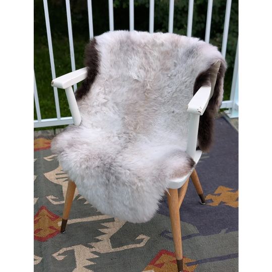 A plush large icelandic sheepskin throw with long wool grayish-brown patches draped on a minimalist chair back by angus oliver