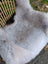 A large icelandic sheepskin rug with long wool, soft white fur, natural grayish tones, and dark edges plush texture