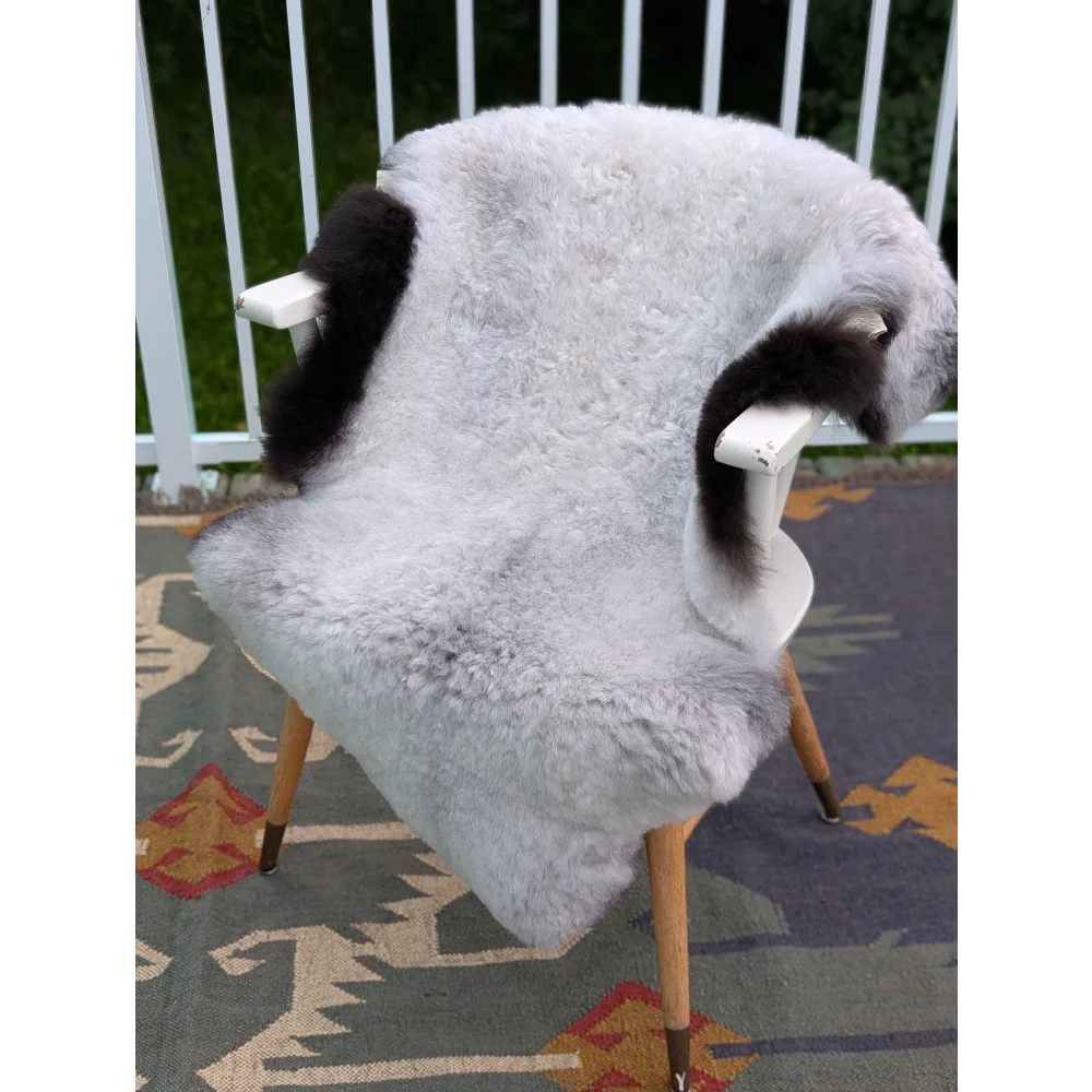 A light gray icelandic sheepskin throw with black fur accents draped over a white wooden chair by angus oliver