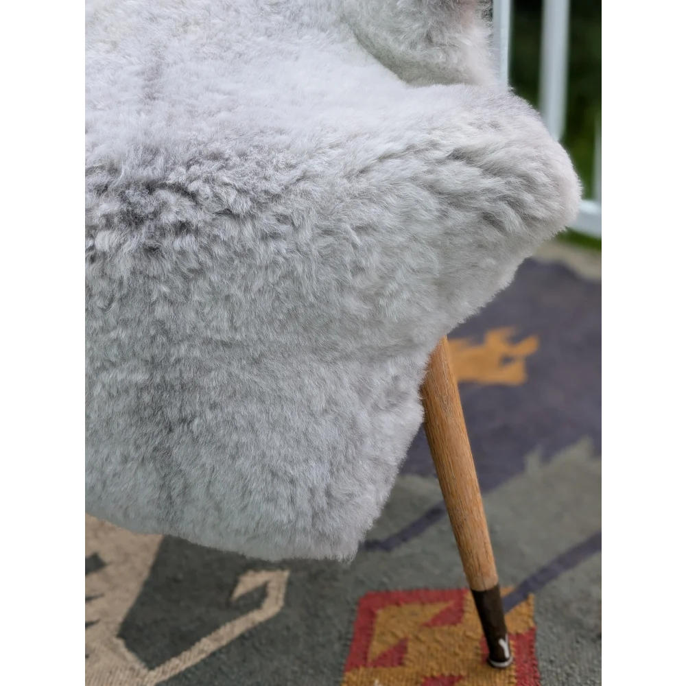 A soft light gray icelandic sheepskin throw with long wool draped over a wooden chair arm by angus oliver