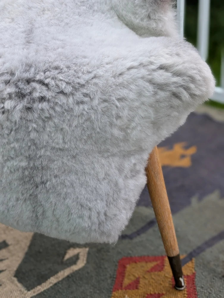 A soft light gray icelandic sheepskin throw with long wool draped over a wooden chair arm by angus oliver