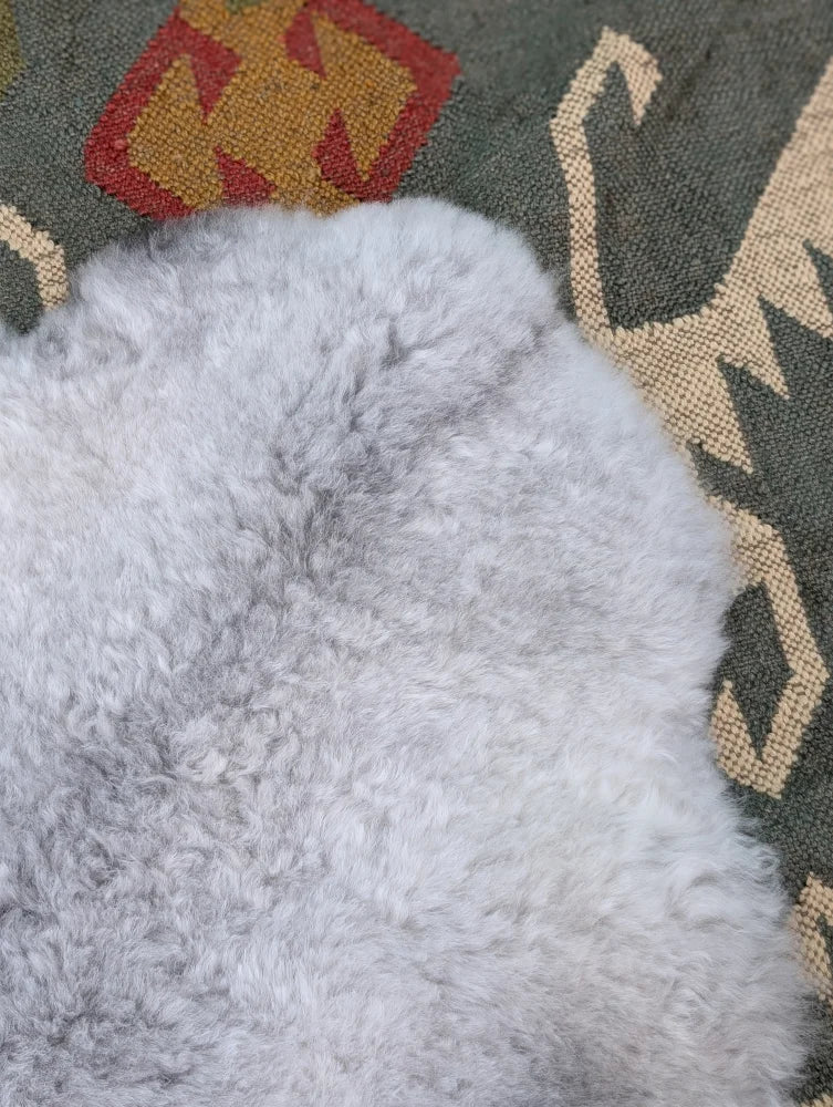 A soft light gray long wool icelandic sheepskin rug with plush curly texture from angus oliver on a patterned carpet