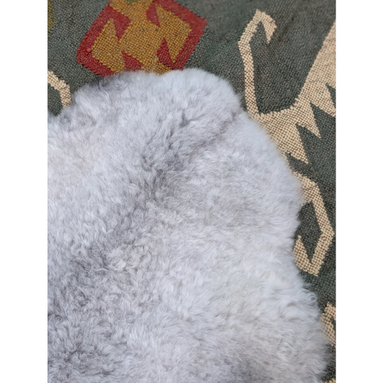 A soft light gray long wool icelandic sheepskin rug with plush curly texture from angus oliver on a patterned carpet