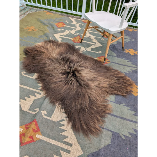 A massive 59 by 37 inch brown icelandic sheepskin rug with long wool texture on a patterned outdoor carpet by angus oliver