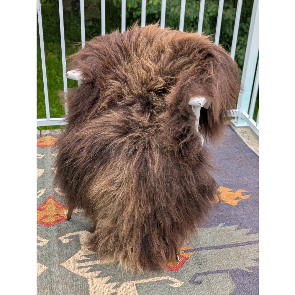 A thick shaggy brown icelandic sheepskin rug with long wool draped over a chair by angus oliver