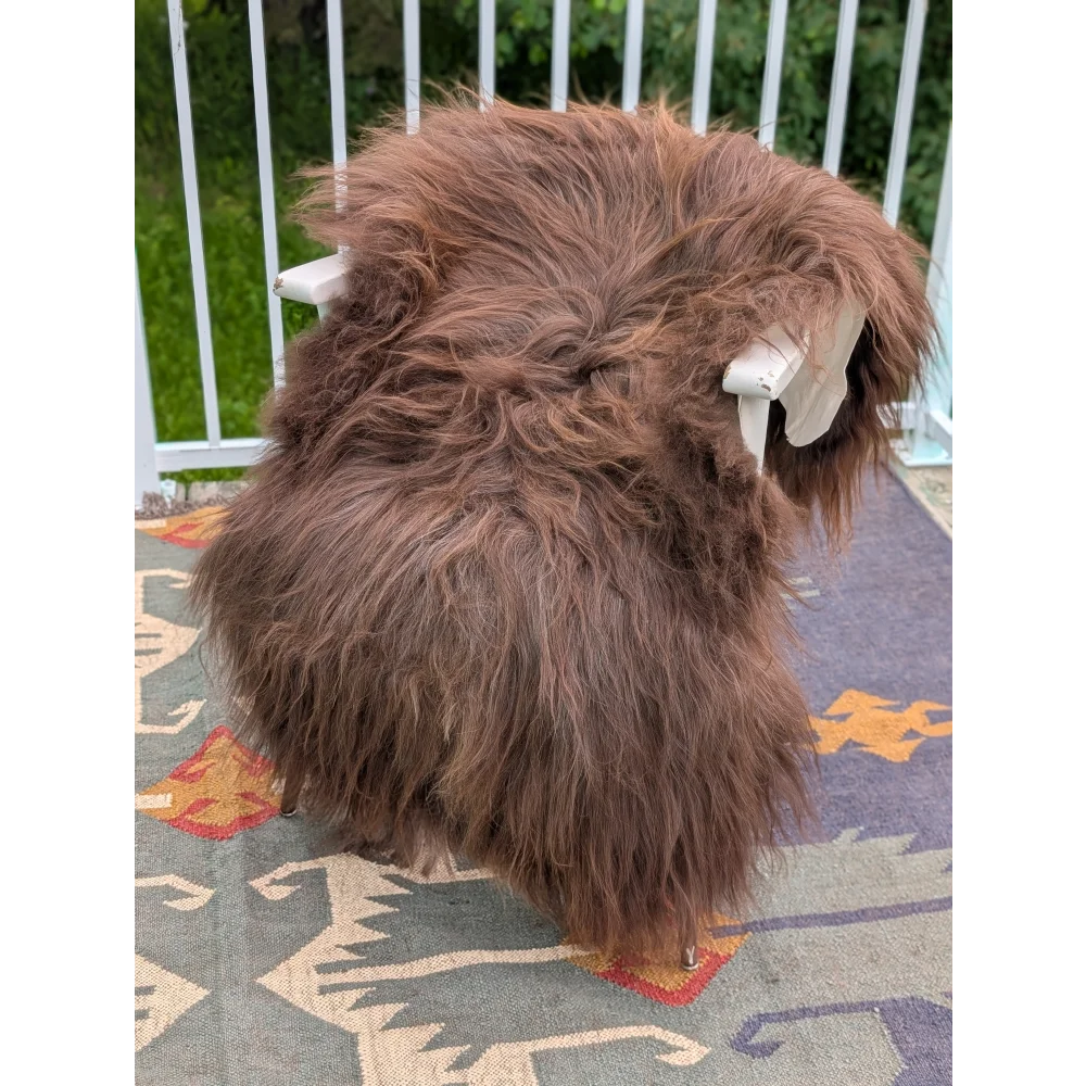 A thick fluffy brown long wool icelandic sheepskin rug draped over a white chair by angus oliver