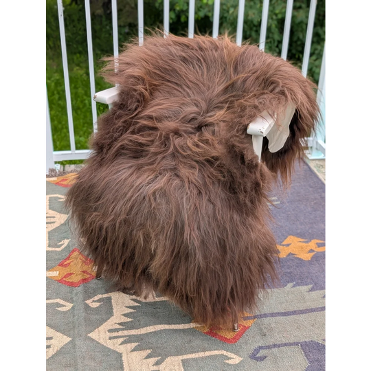 A thick fluffy brown long wool icelandic sheepskin rug draped over a white chair by angus oliver