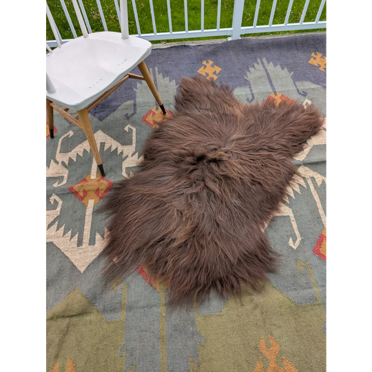A plush brown long wool icelandic sheepskin rug by angus oliver lying on a patterned carpet measuring 58 by 35 inches