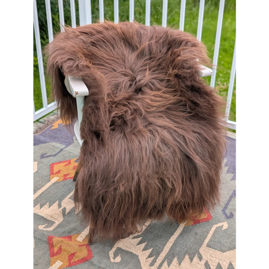 A thick fluffy brown icelandic sheepskin rug with long wool draped over a white chair by angus oliver
